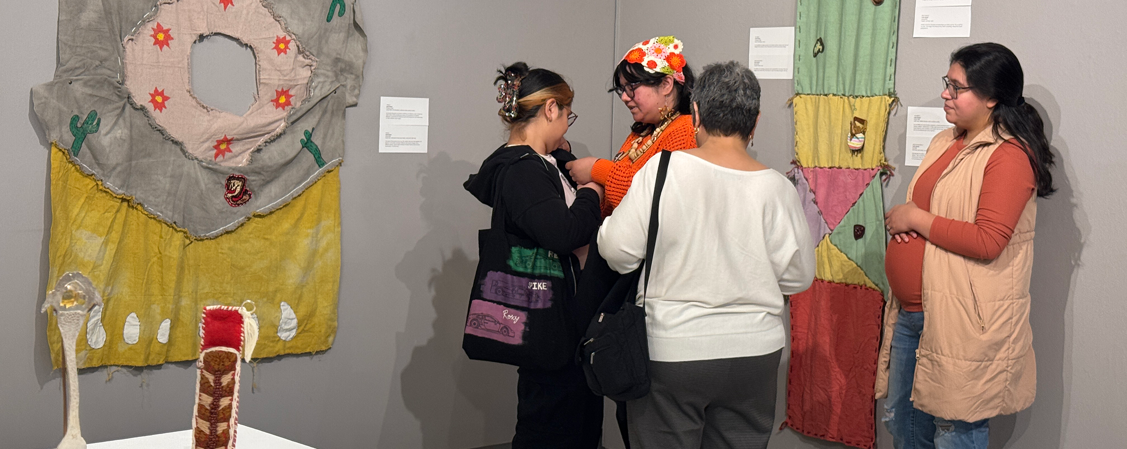 People stand in the Crossman Gallery with colorful fabrics hanging on the walls.