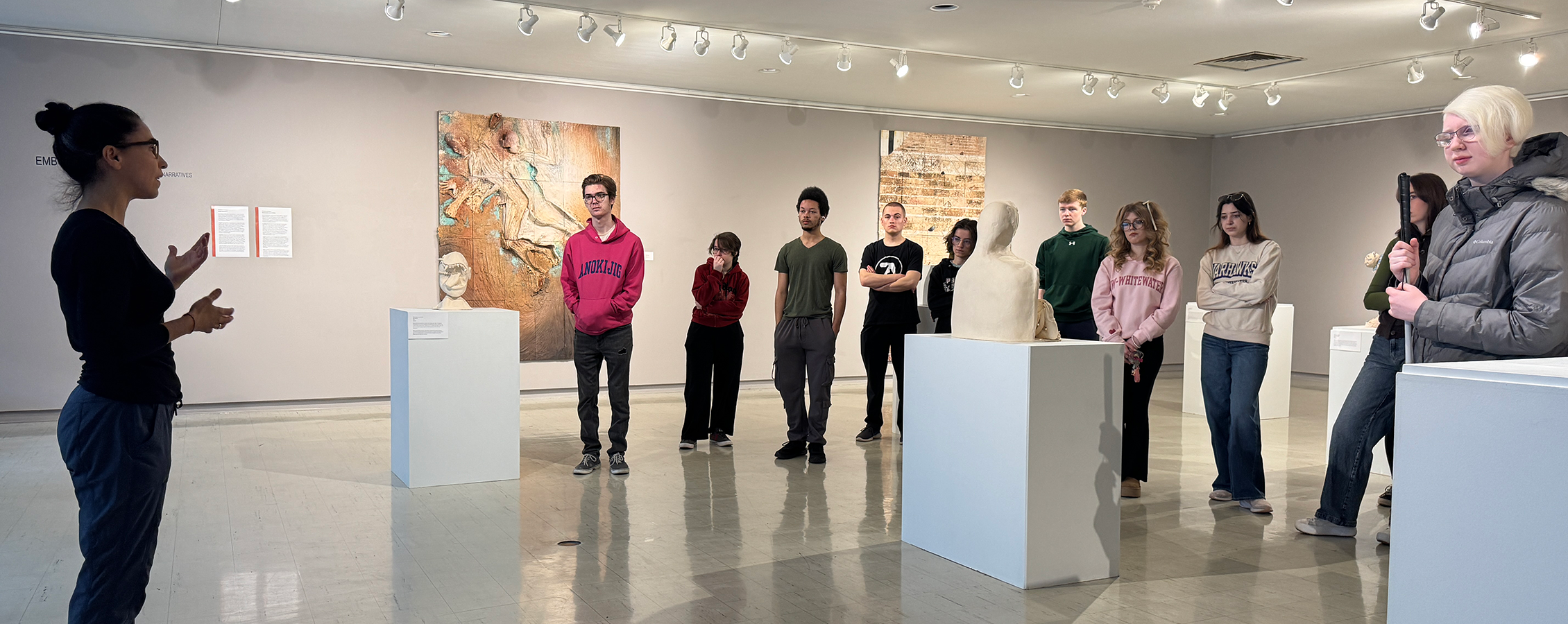A group of people gather in the Crossman Gallery with one person speaking at the front of the gallery.