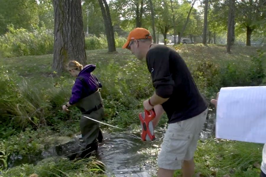 An instructor and a student use a measuring tool in a stream.
