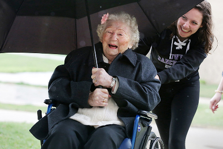 A young person pushes an older person in a wheelchair.