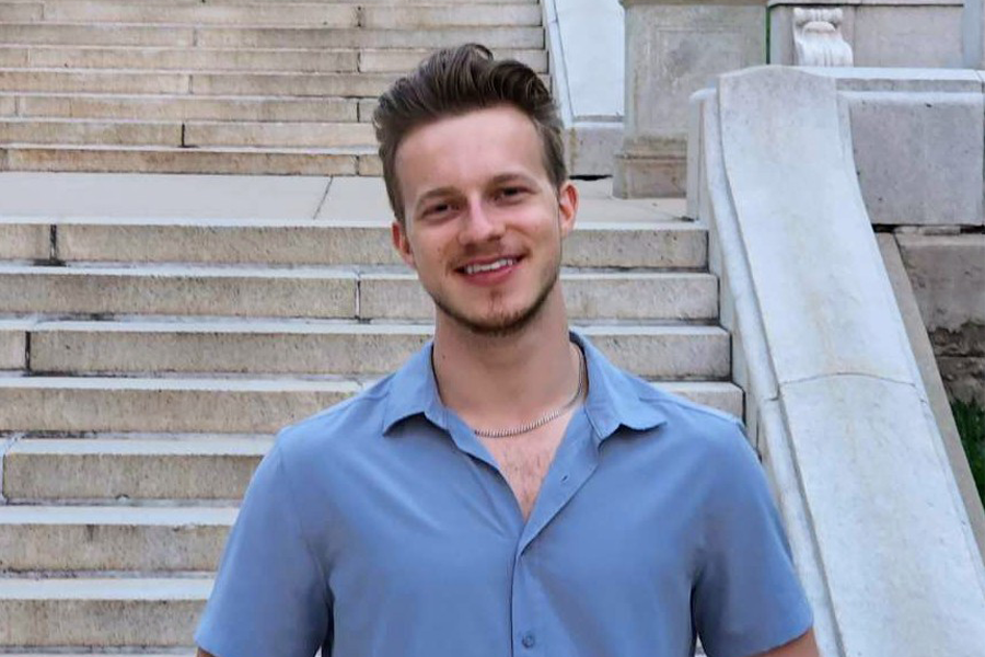 Owen Gaber smiles in a blue shirt standing in front of concrete stairs.