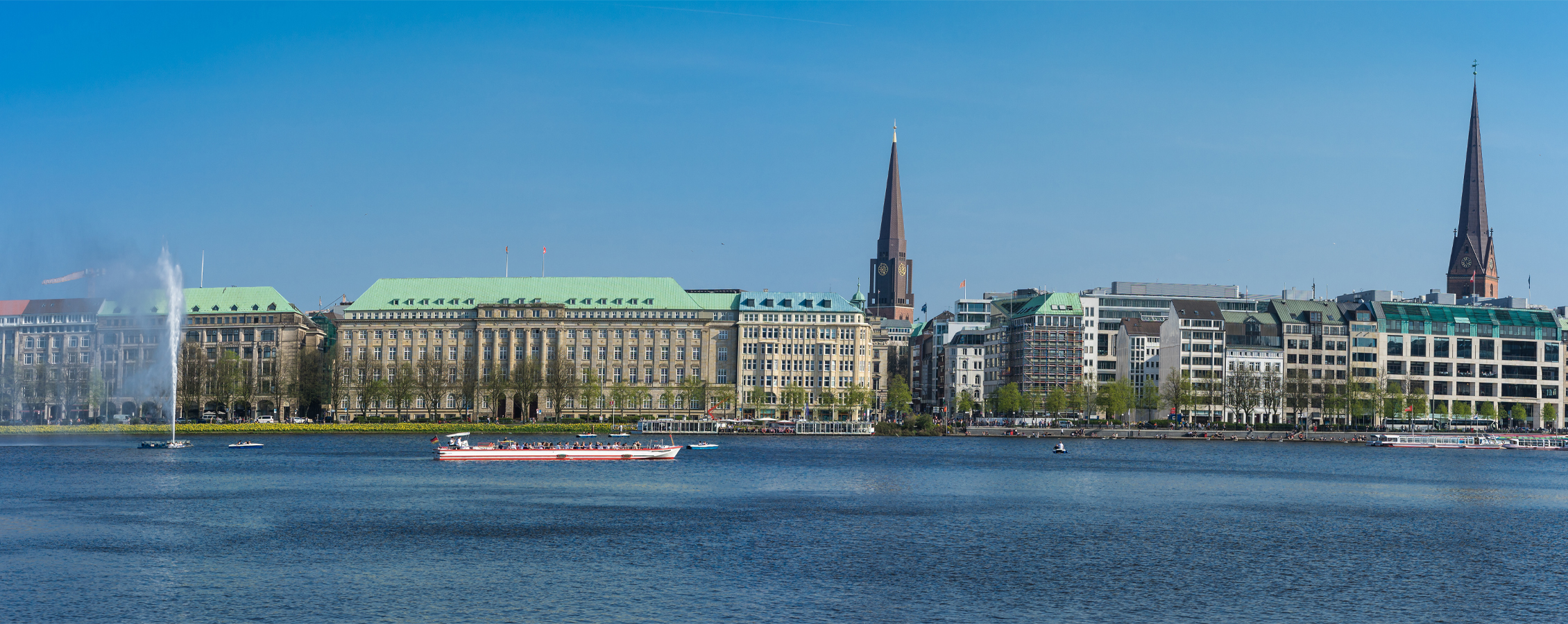 A red and white boat travels down a river through a city in Germany.