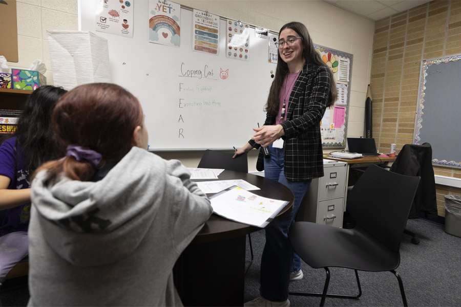A school psychology student stands in front of a white board with children in the foreground.