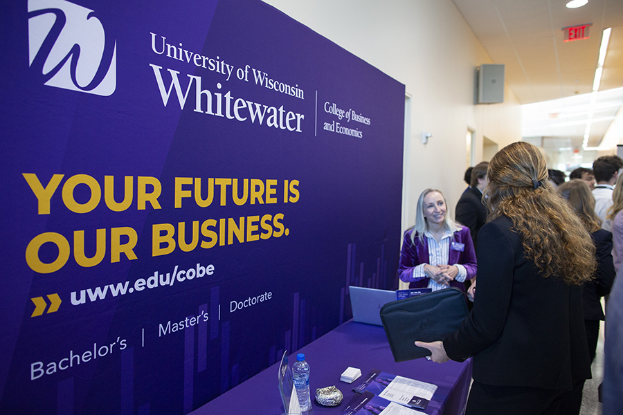 Two people talk by a purple sign that says Your Future is our Business.