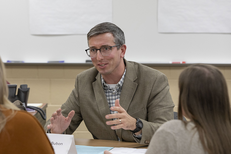 A faculty member wearing a blazer faces two people that have their backs to the camera.