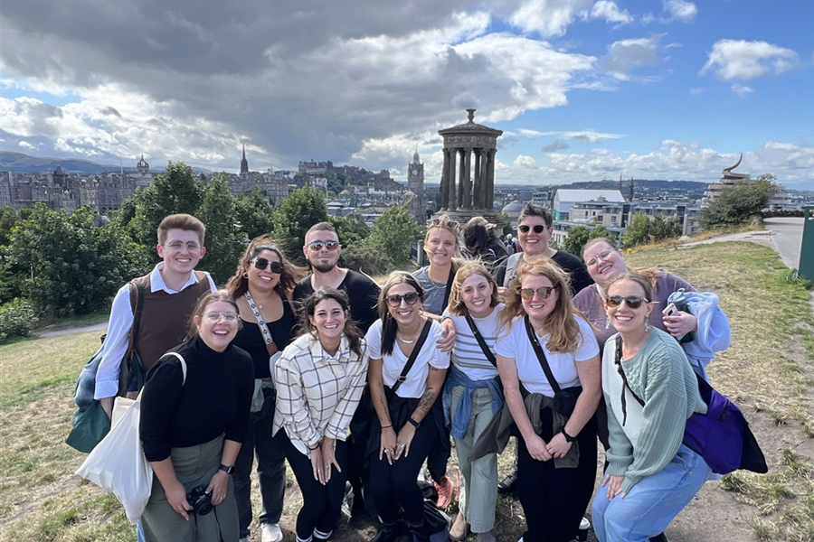 A group photo taken outdoors on a hill in Scotland overlooking a city.