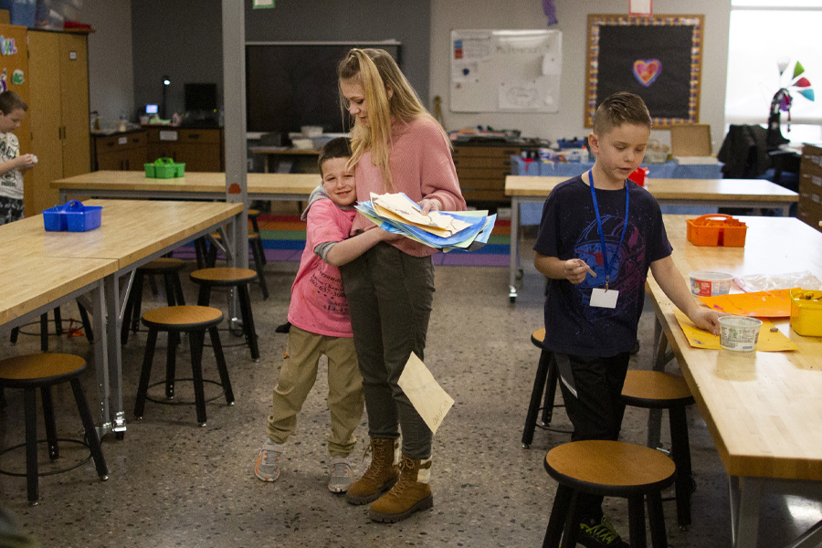 A student teacher sits amongst high schoolers and performs a demonstration on paper.