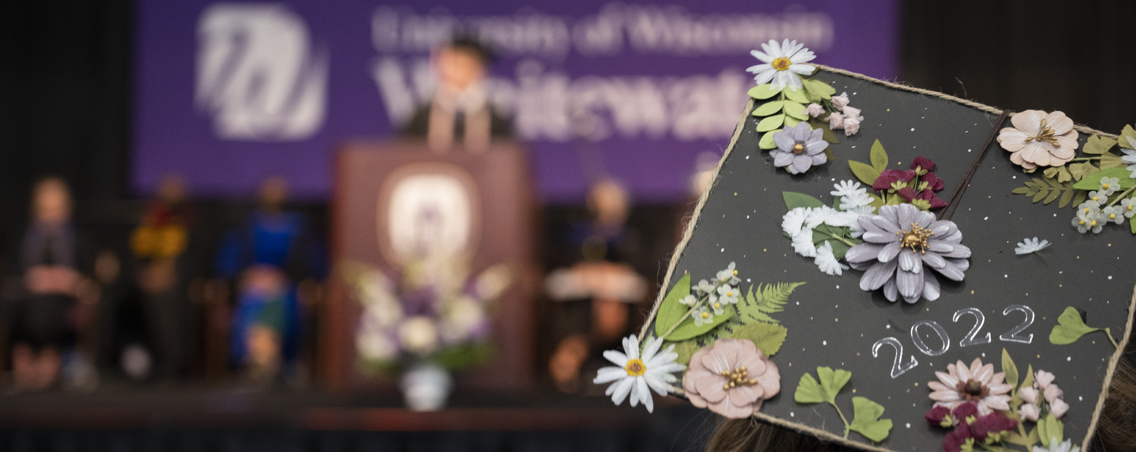 The back of a decorated graduation cap with a UW-Whitewater banner in the background. 