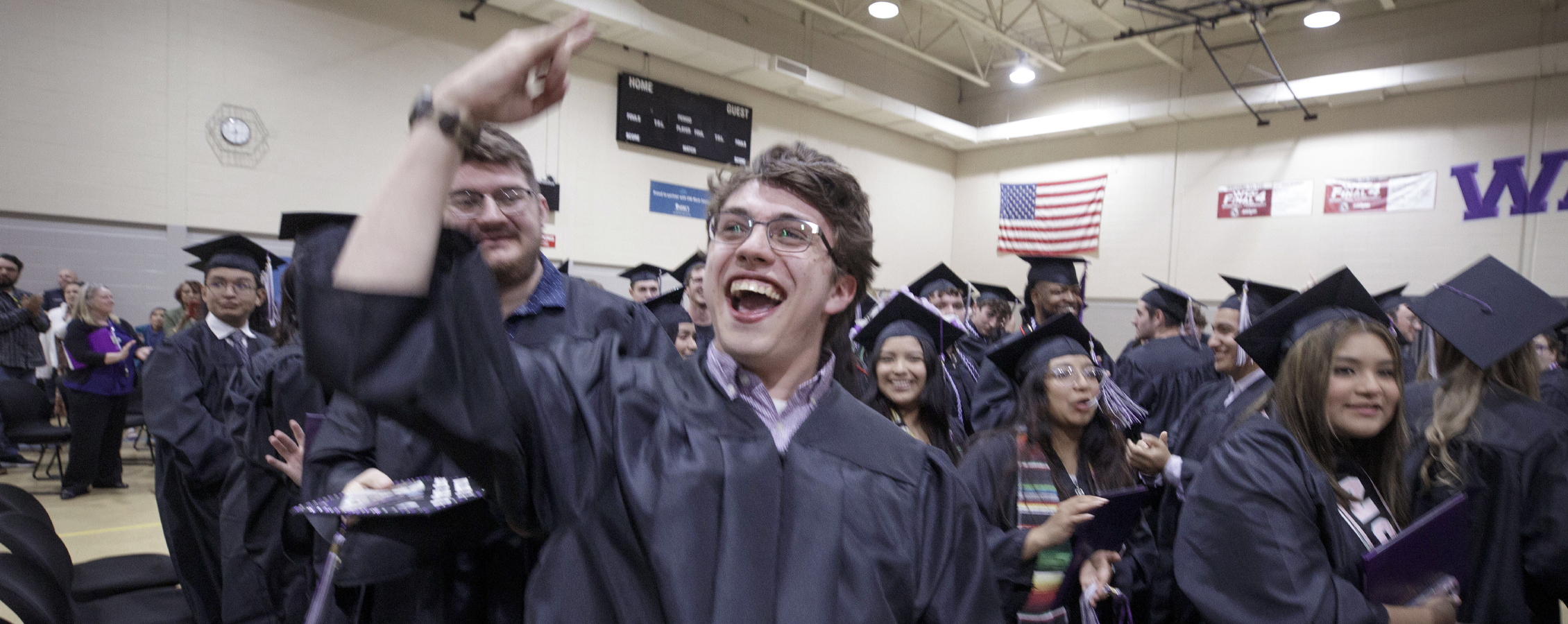 Students wearing graduation regalia celebrate indoors on the Rock County campus.