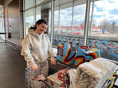 Student stands in Aldi behind a cart wearing a grey hooded sweatshirt