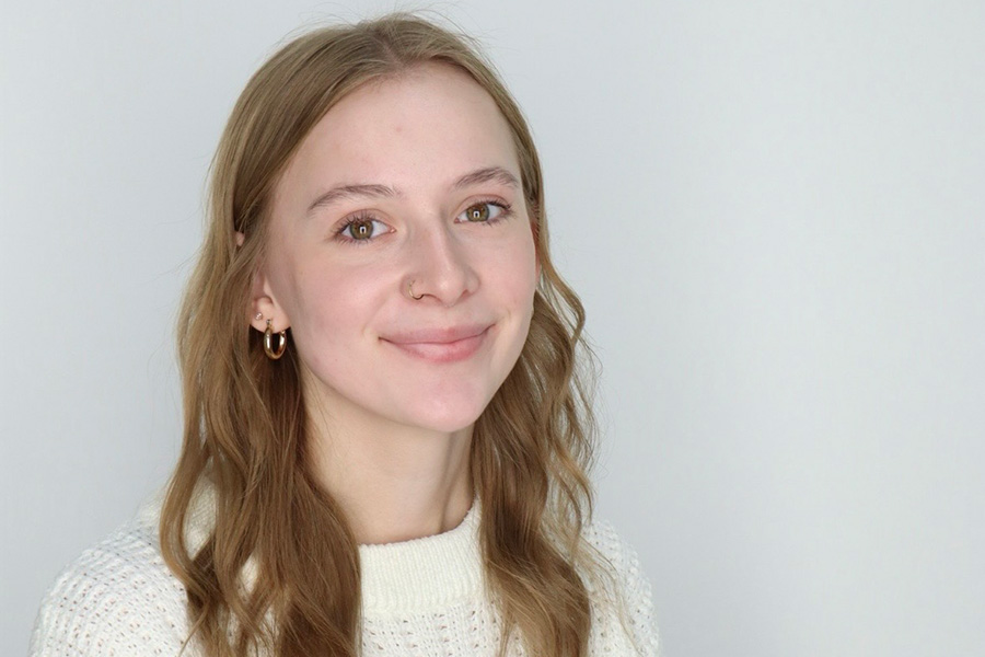 Alaina Jones wearing a white sweater sitting in front of a grey background.
