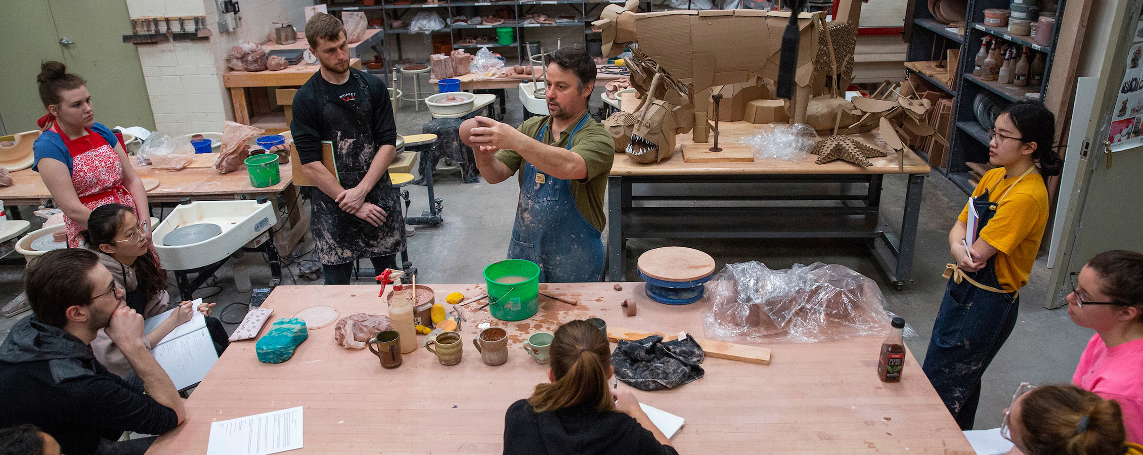 Instructor teaching students ceramics class in art studio with large table