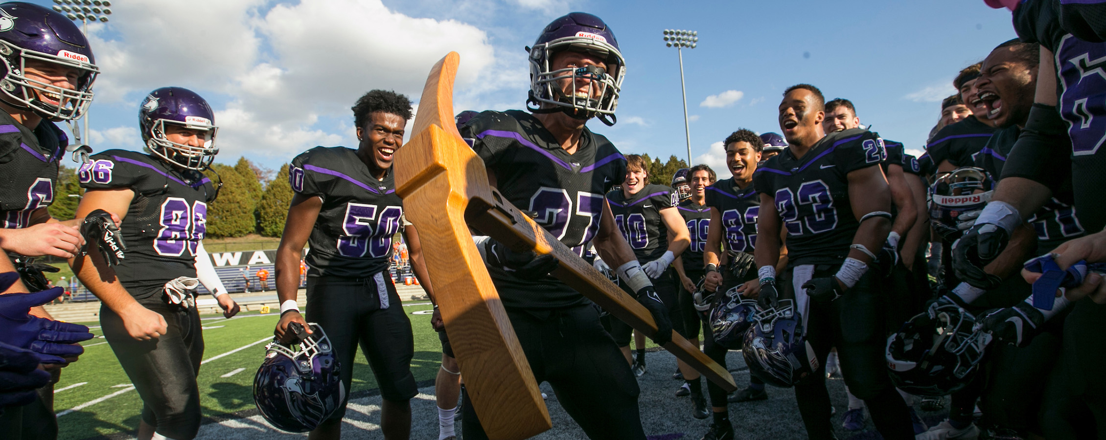 UW-Whitewater football players celebrate in their purple uniforms with a trophy