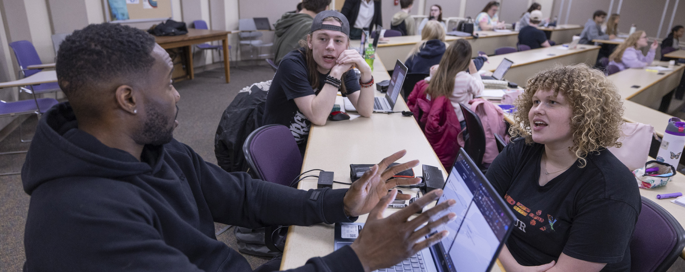 Three students have a group discussion in a classroom.