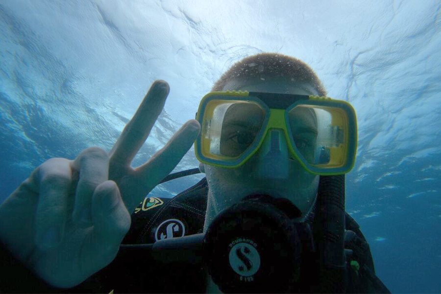 An underwater shot of a student wearing scuba gear makes a peace sign with his fingers.