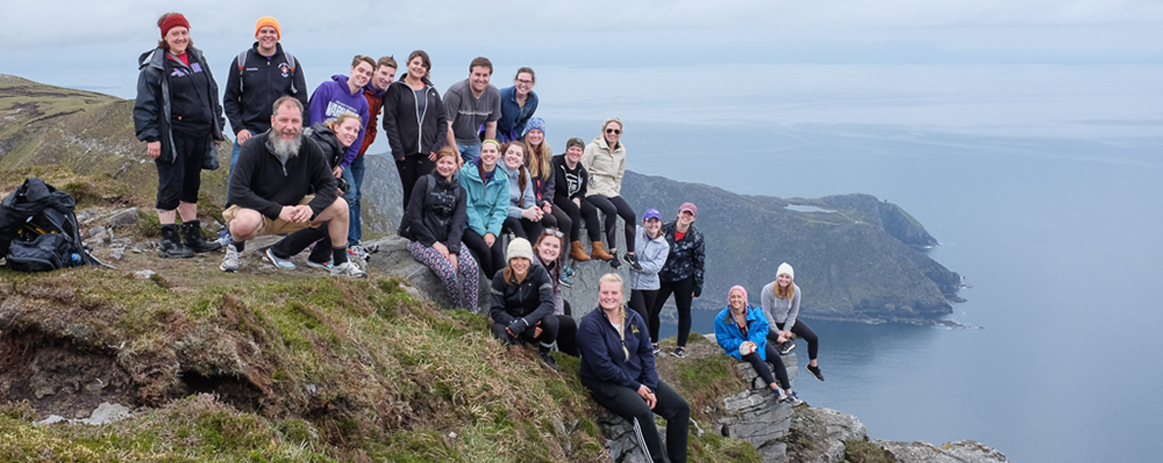 Students and a faculty member sit along the edge of a cliff overlooking the sea.