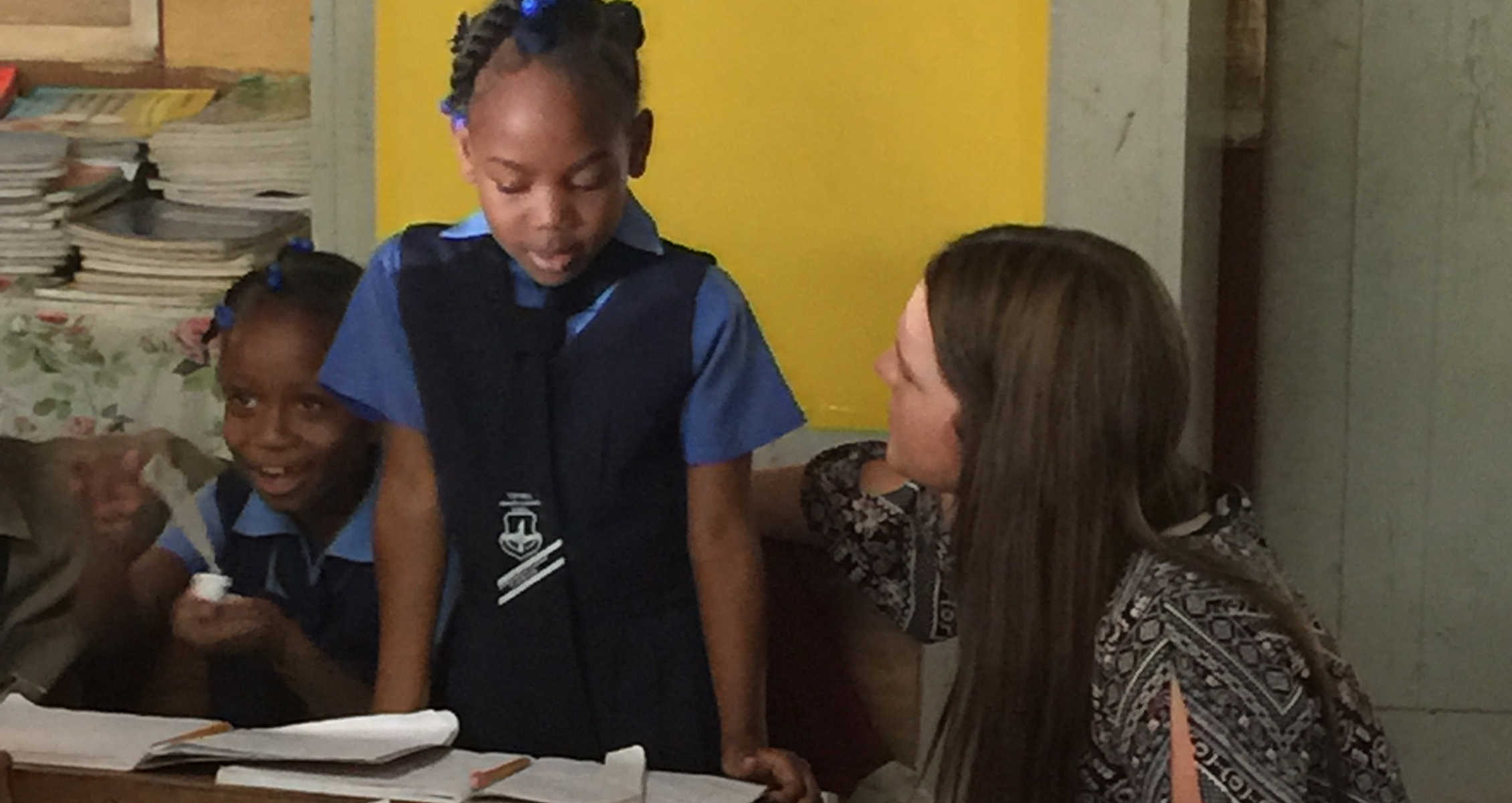 A UW-Whitewater student kneels by two Jamaican girls in a Jamacian classroom.