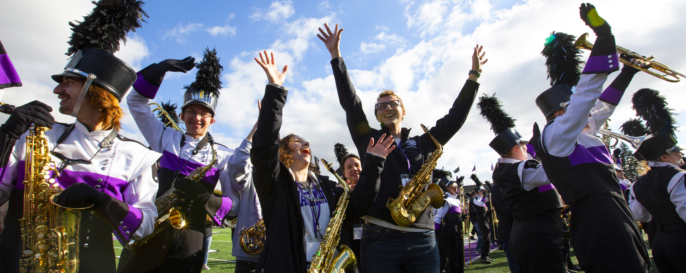 Marching Band members celebrate with their instruments and hands in the air.