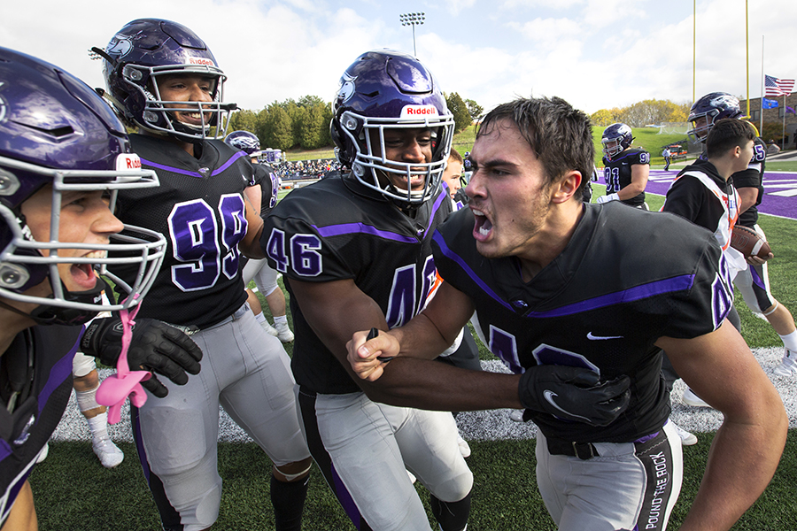 Four Warhawk football players celebrate on the sidelines.