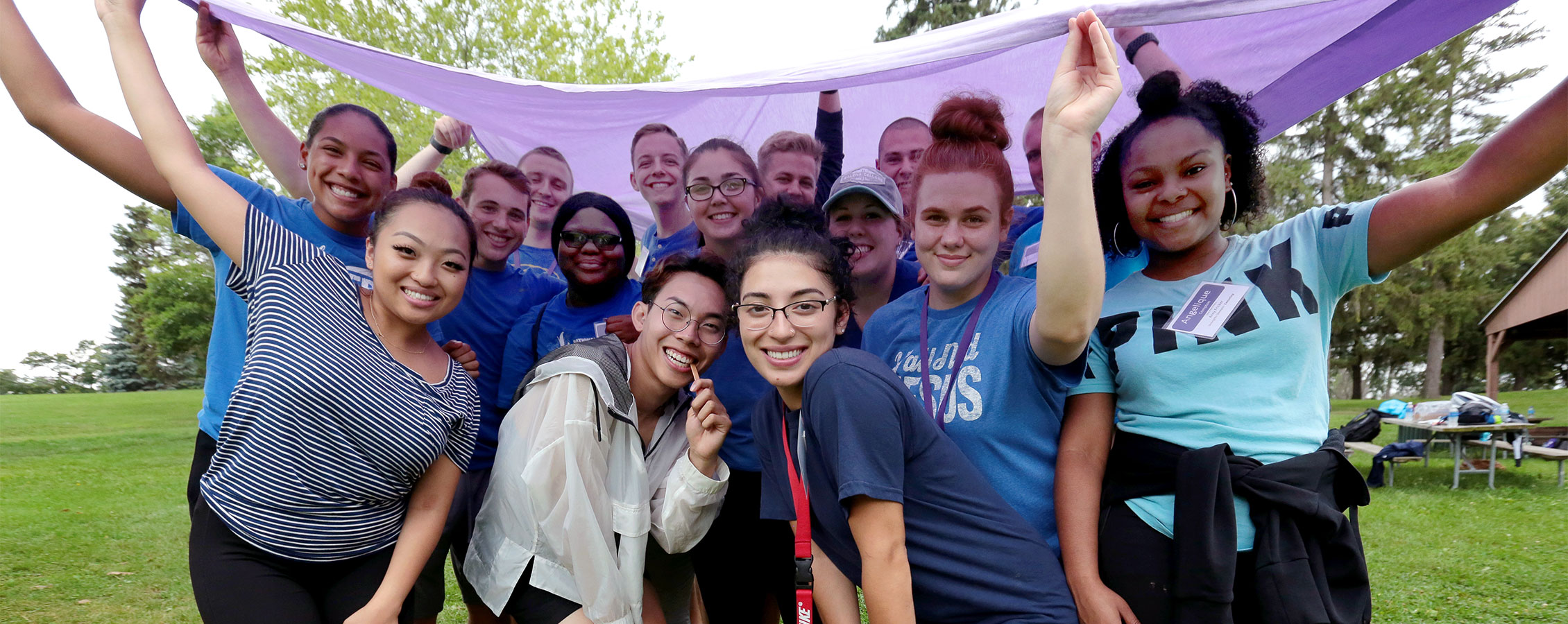 UW-Whitewater students huddled under a purple flag in front of a housing building.