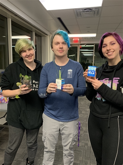 Three students holding plants potted in milk cartons and water bottles