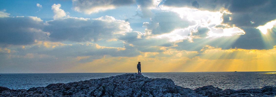 A person stands on a mountain by the sea.