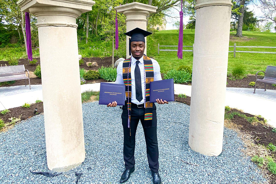 A student stands in front of the columns with two diplomas.