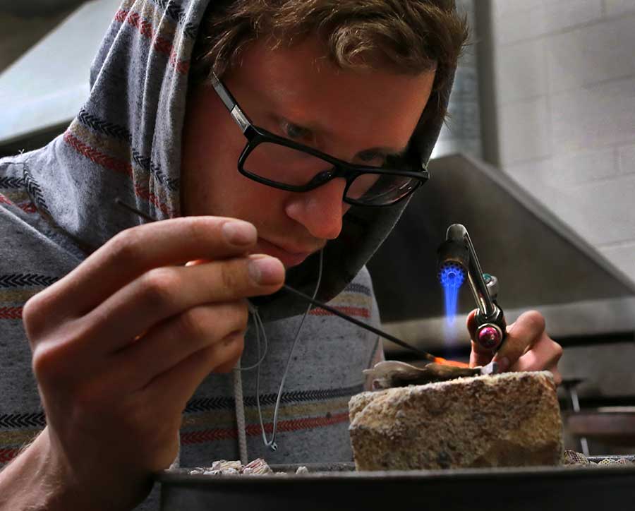 A student creates jewelry with a flame.