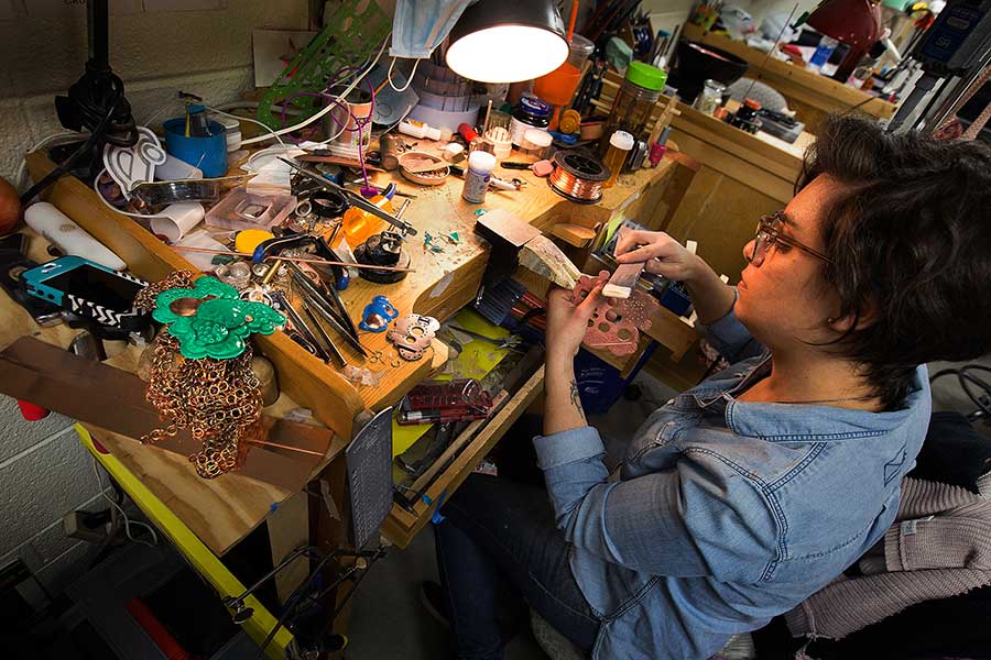 A student works at a wooden table covered in tools and materials.