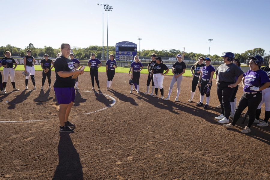 Brenda Volk stands in the infield of a ball diamond, surrounded by her team wearing softball uniforms.