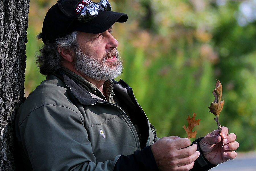 Tony Gulig standing with his back against a tree holding two leaves.