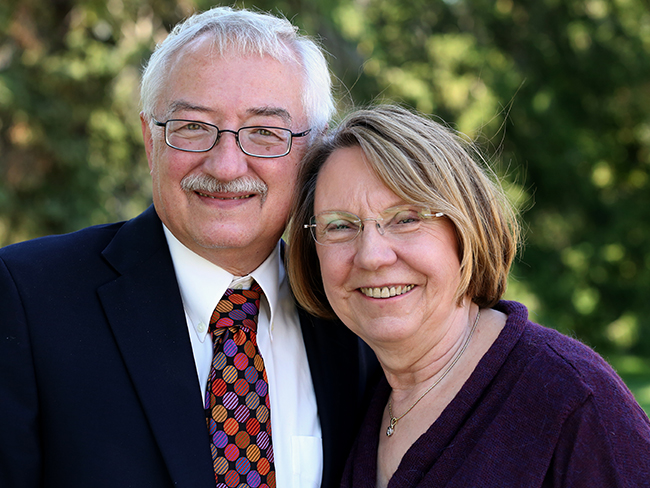 Annette and Dale Schuh hug and smile at the camera with trees in the background.