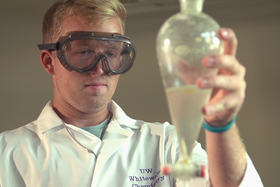 A student looks a vial while wearing safety goggles.