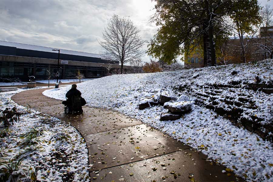 A student in a wheelchair travels along a sidewalk on campus.