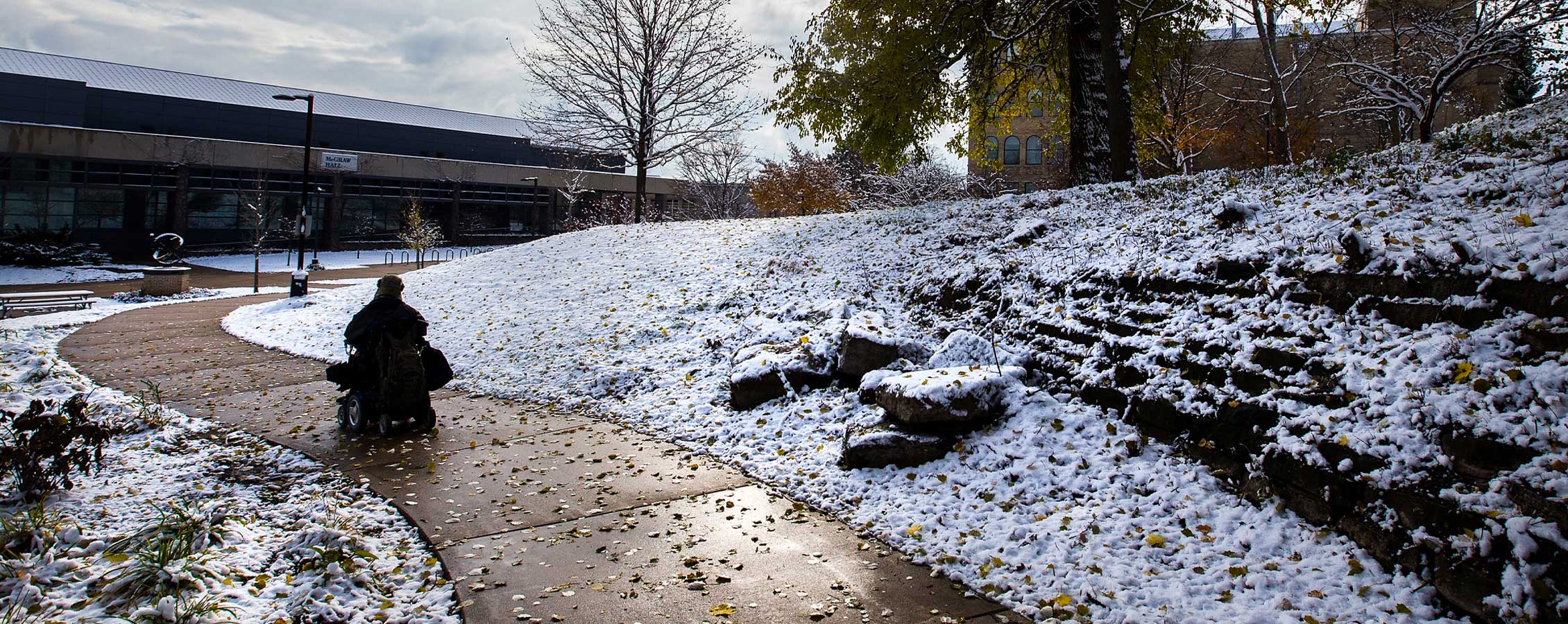 A student in a wheelchair travels along a sidewalk on the UW-Whitewater campus.