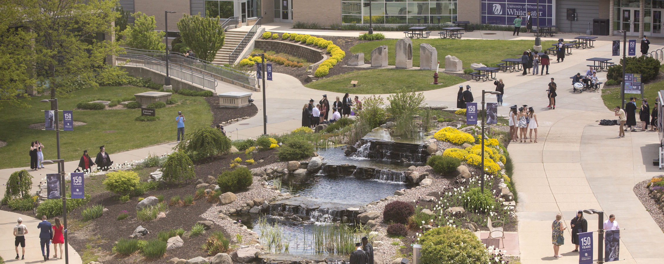 Graduates walk around the water feature.