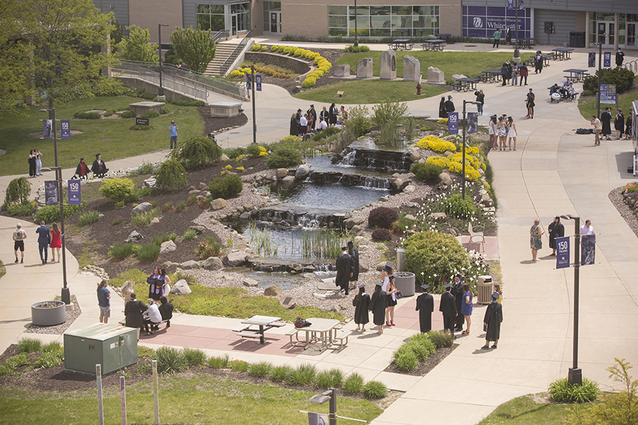 Graduates walk around the water feature.