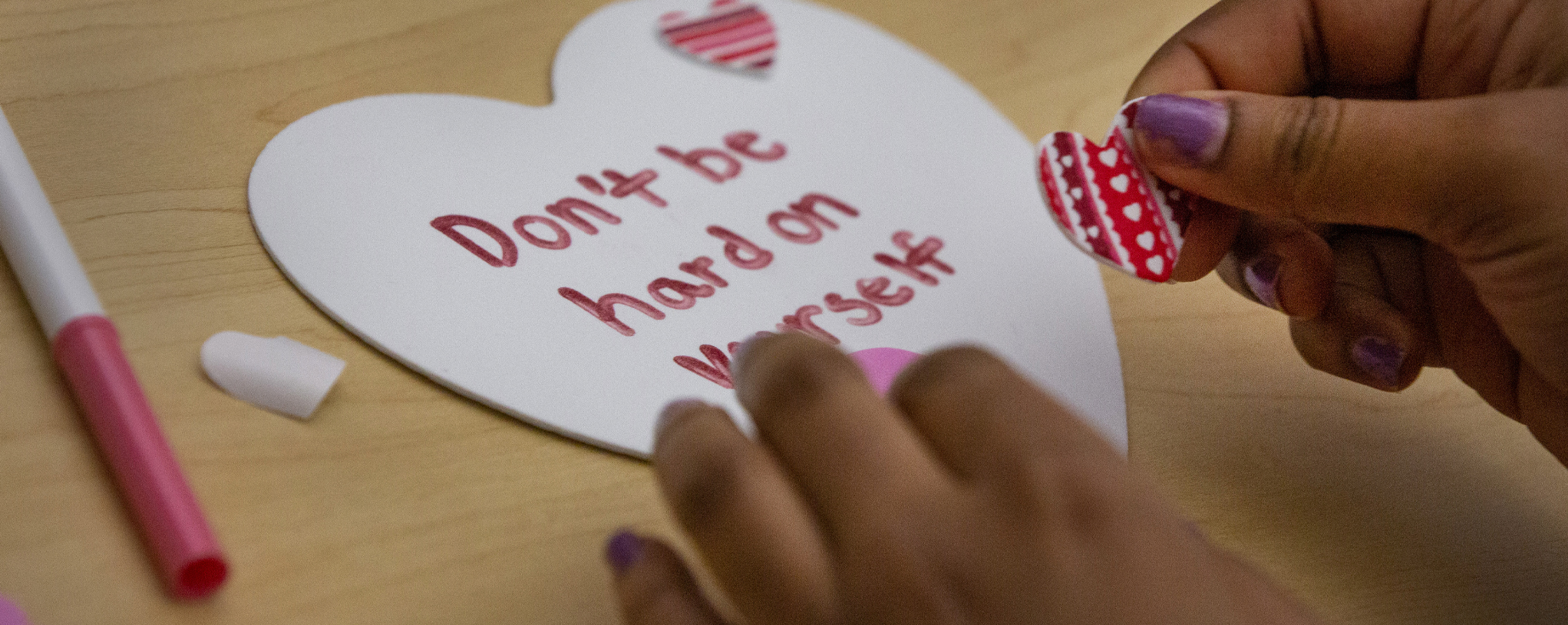 Person decorates a paper heart, says don't be so hard on yourself.