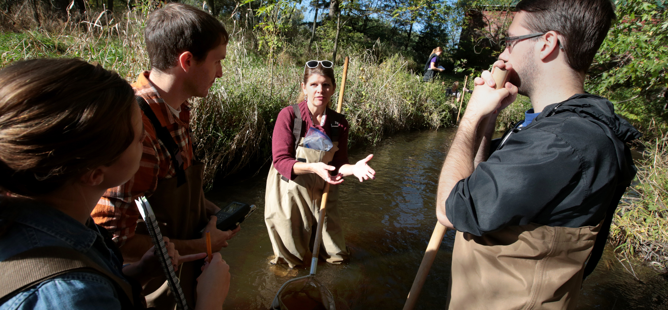 Associate Professor Elisabeth Harrahy stands in a river talking to students.