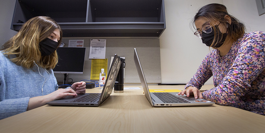 Two students on their laptops sit at a table.