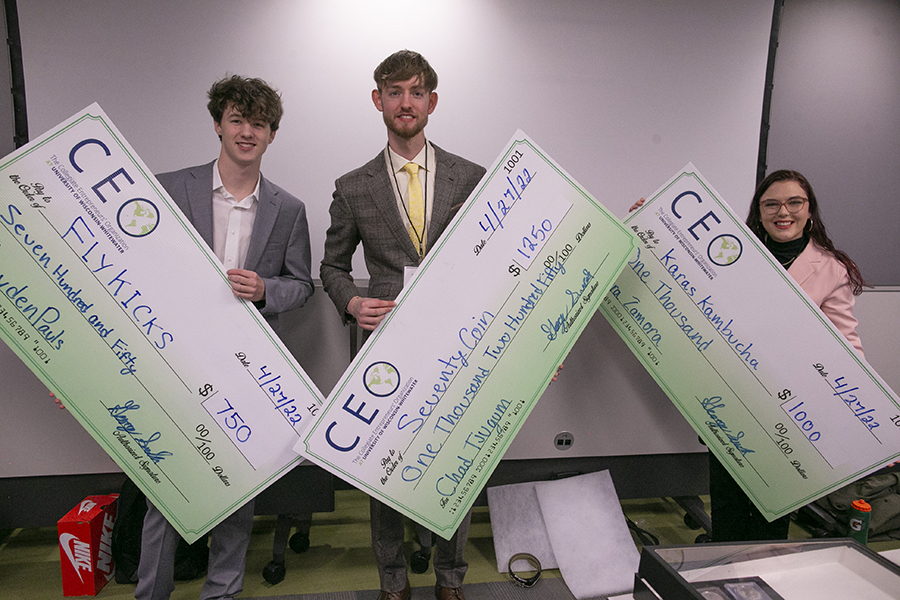 Three students hold large checks