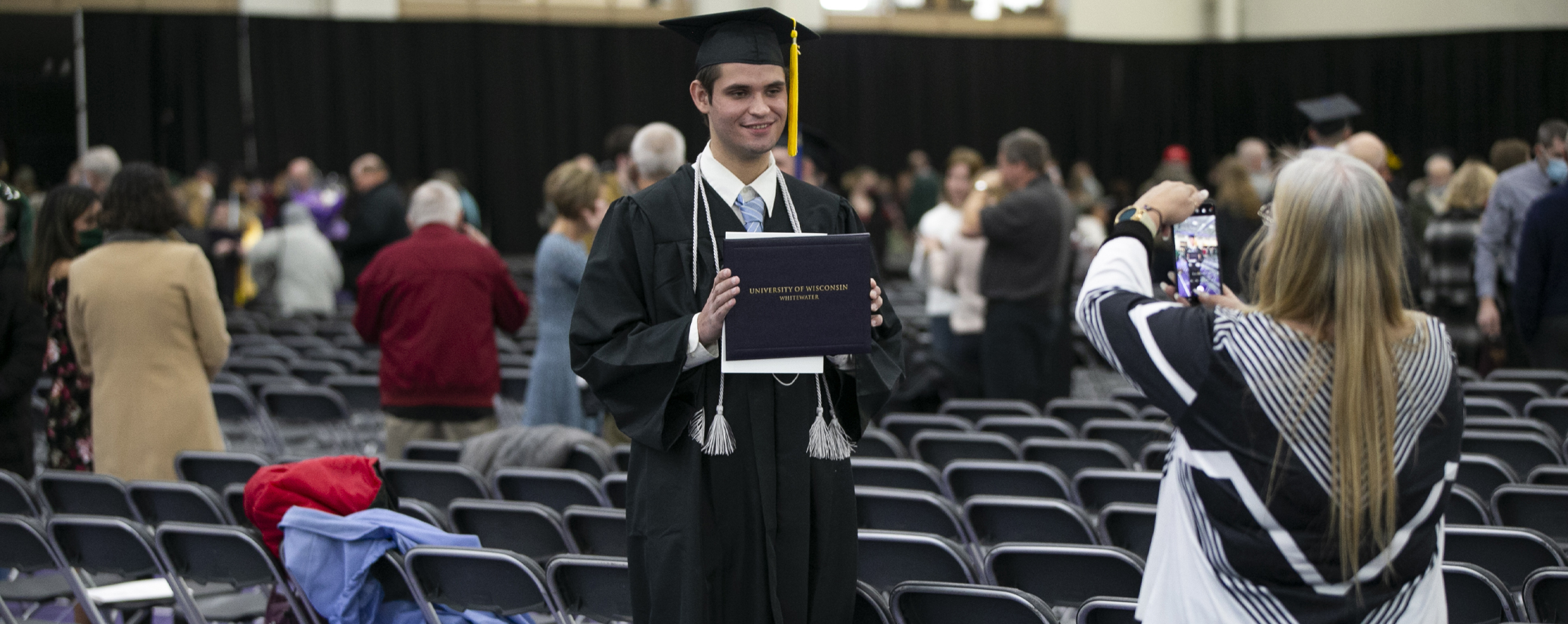 A graduate stands with their diploma and gets their picture taken.