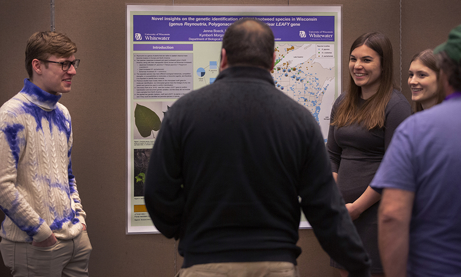 Three students and a faculty member stand by a research poster regarding knotweed.
