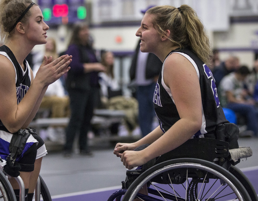 Two female wheelchair basketball athletes talk to each other on the court.