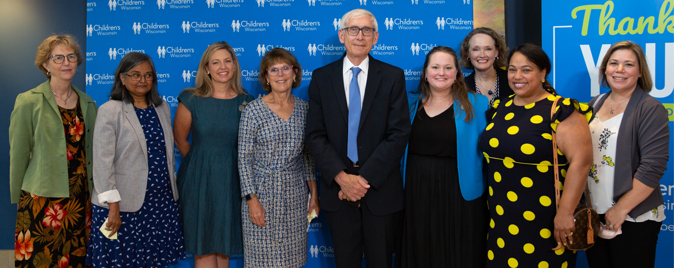 Governor Tony Evers stands with other professionals in front of a blue Children's Hospital backdrop.