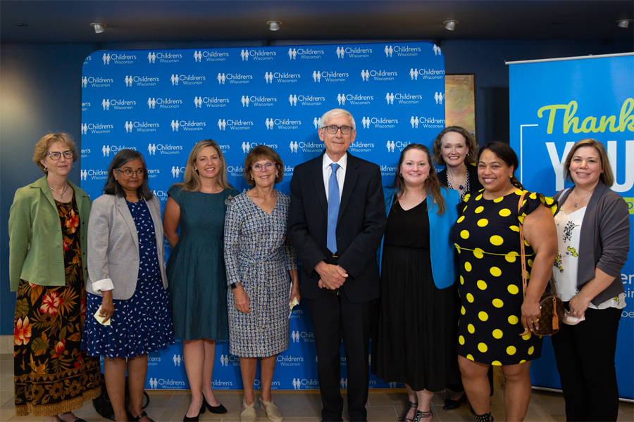 Governor Tony Evers stands with other professionals in front of a blue Children's Hospital backdrop.