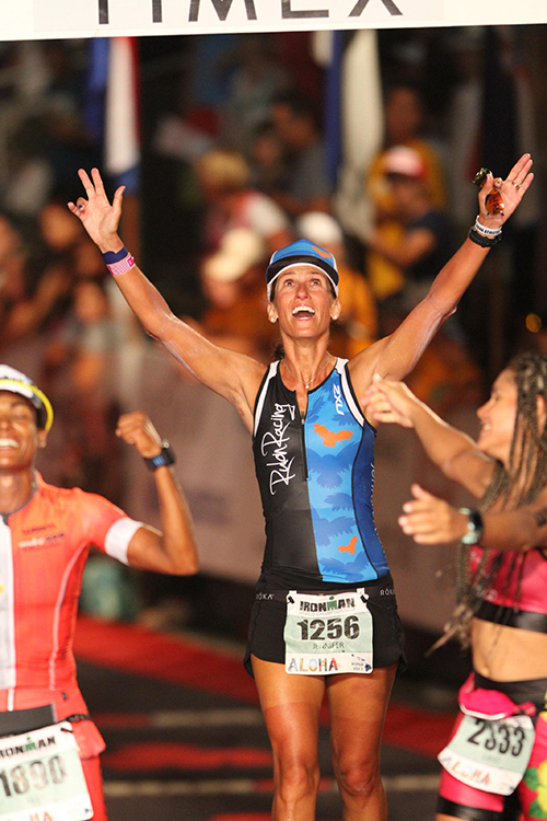 Jen Rulon dressed in running hear throws her arms up with a smile on her face during a race.