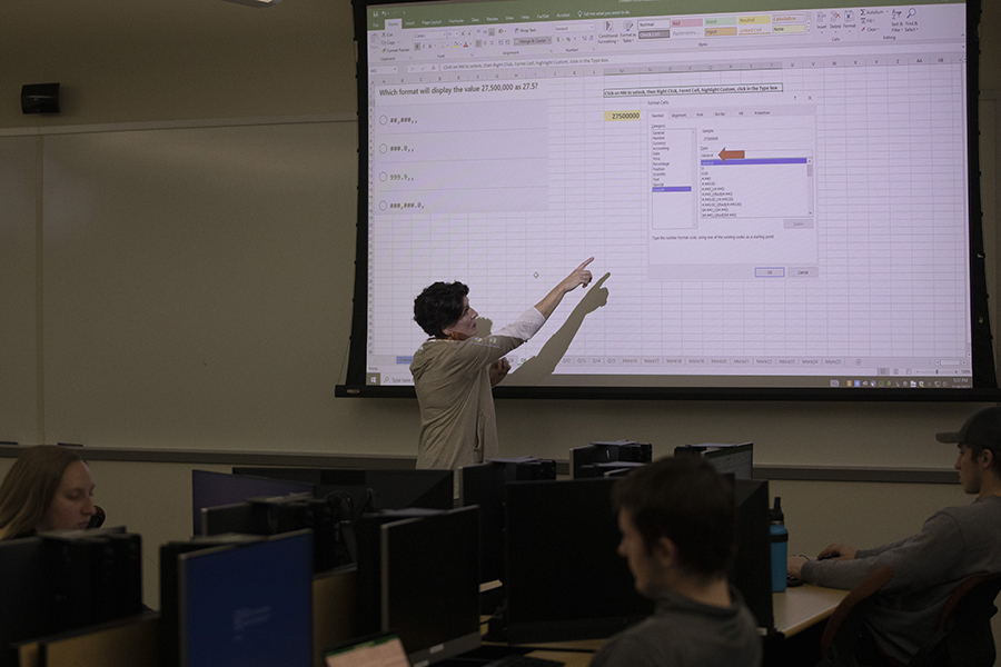 Advisor Linda Amann points at an Excel document shown on a projector screen.