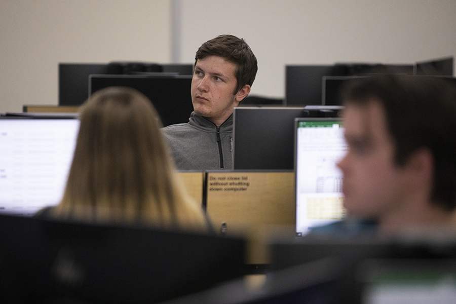 A student sits amoungst computers facing the camera looking to his right.