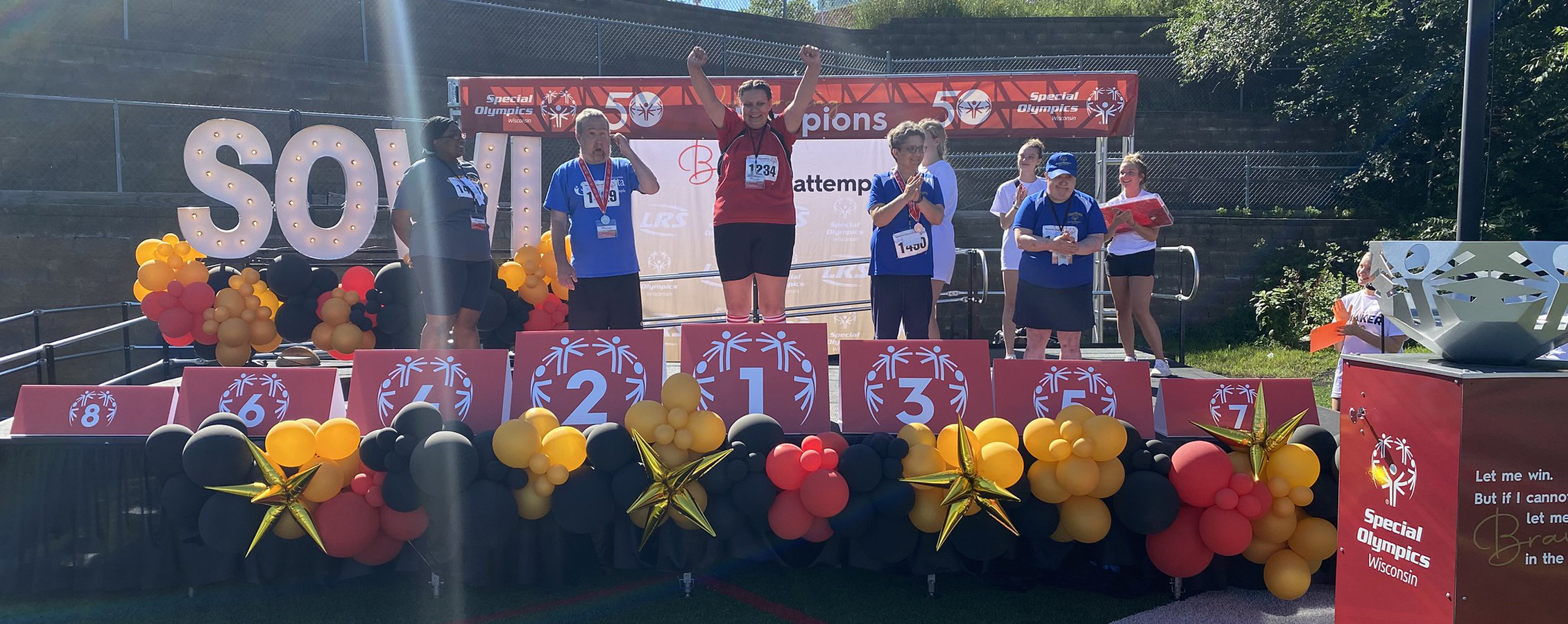 Special Olympics participants stand on a stage and celebrate.